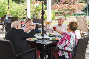 Four seniors seated at a patio table enjoying food and wine