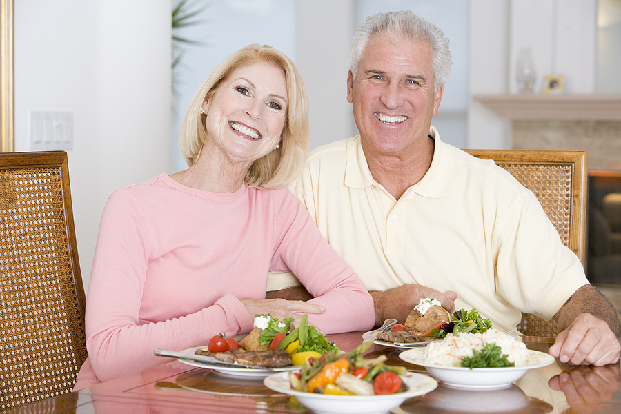 A senior couple sits at a table with healthy food.