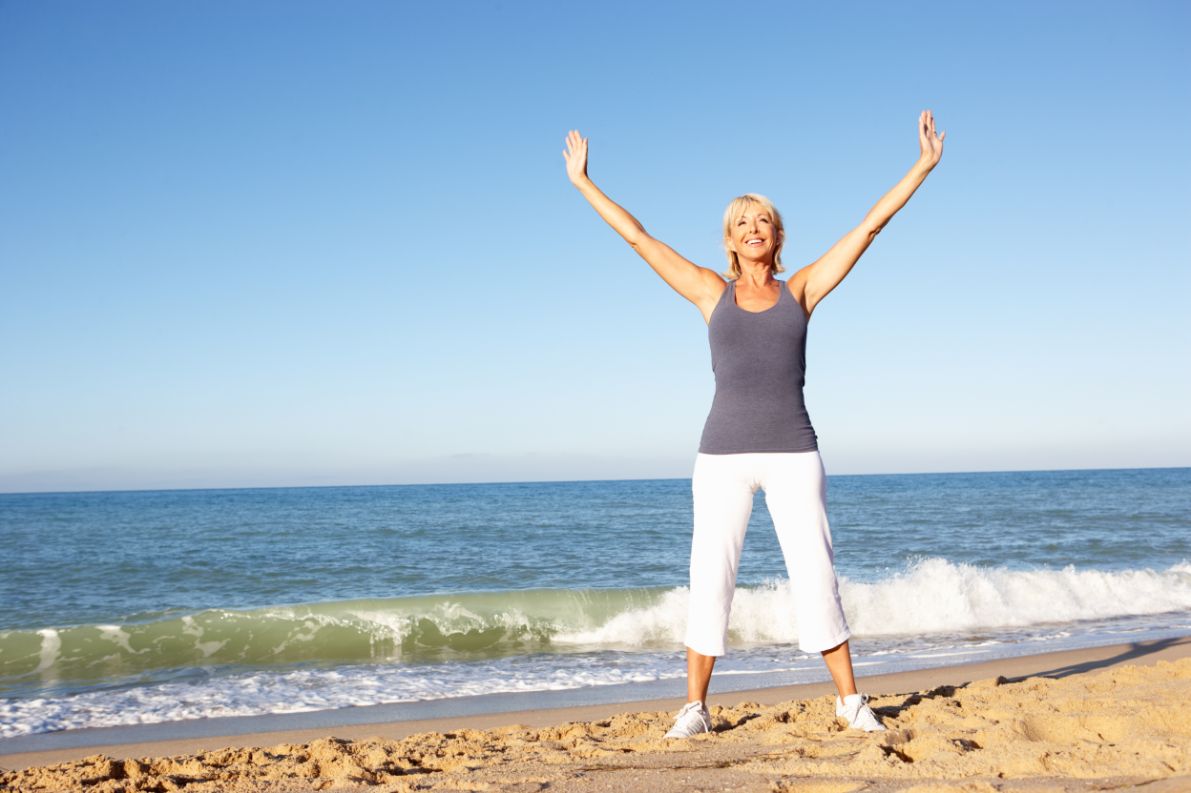 A senior woman stretches on the beach for knee and hip pain relief.