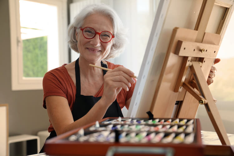 A senior woman enjoys painting as an indoor hobby.