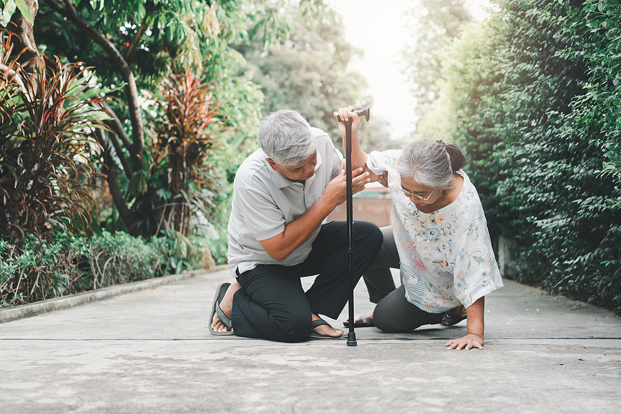 A senior man helps a senior woman who has fallen on a path
