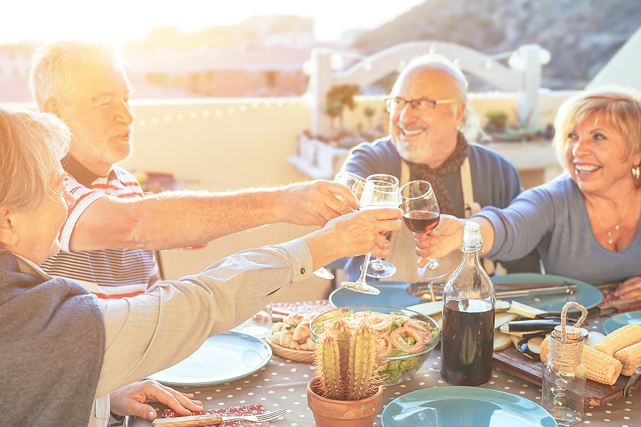 A group of older adults cheering with red wine at a dinner table