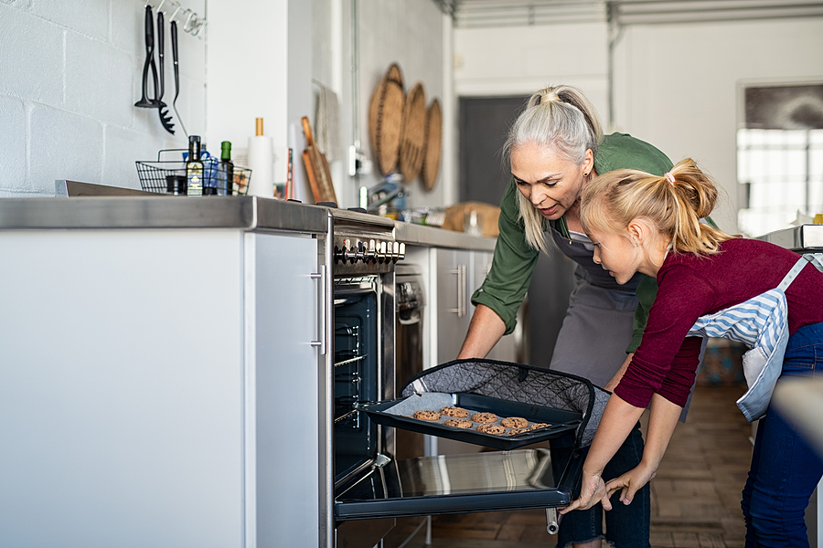 Grandmother and granddaughter are taking cookies out of the oven.