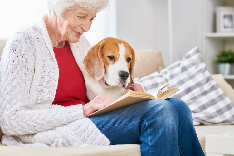Senior woman reading on the couch with her dog in a pet-friendly senior living community.