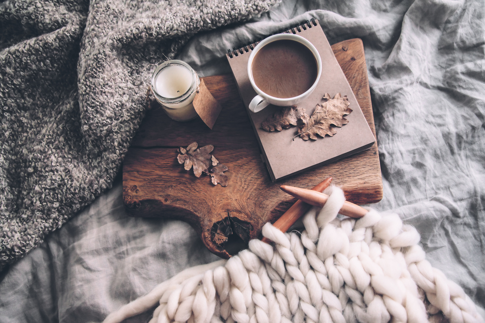 Large cable knit knitting, a candle, leaves, and a blanket for a hygge feel