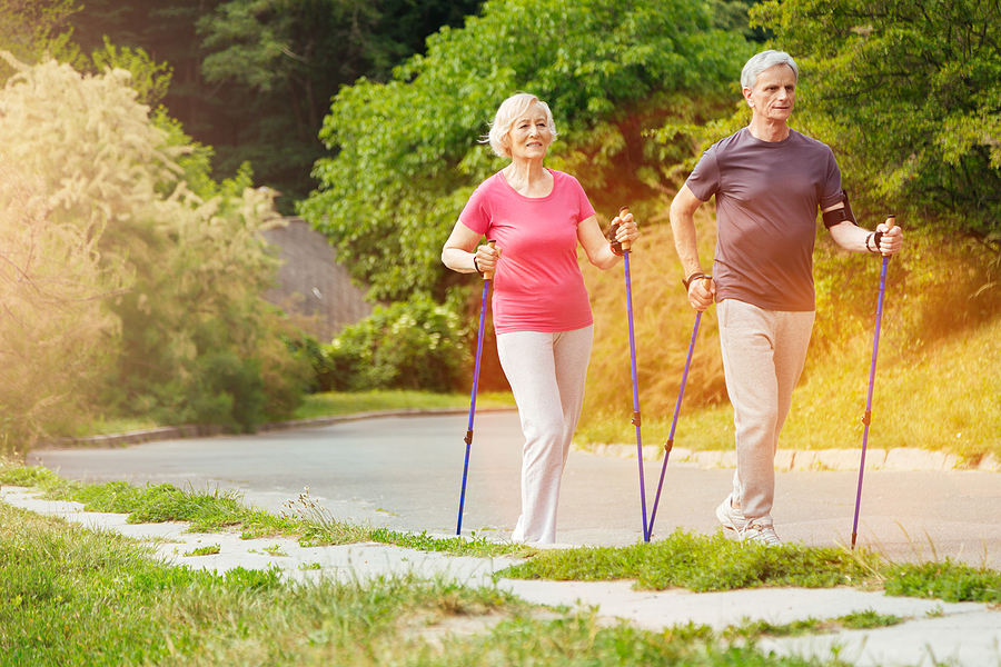 A senior couple walks along a path using poles.