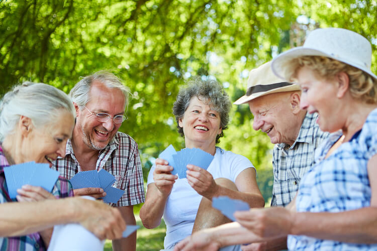 Group of senior friends playing cards outside of their continuing care retirement community.