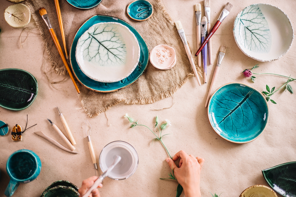 Older hands work on painting and adding glaze to pottery pieces on the table